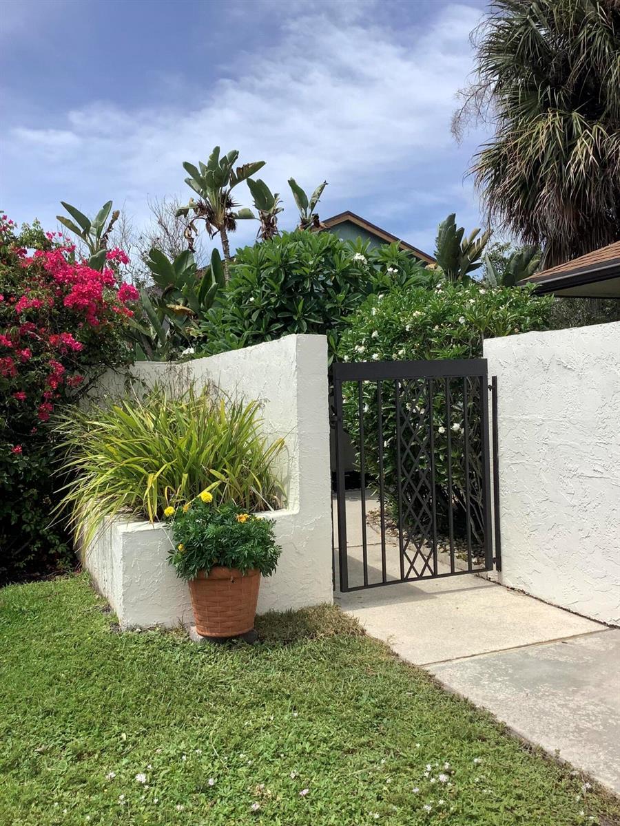 A white stucco wall with a black metal gate and a potted plant outside — 458 SW 29th Avenue, Delray Beach FL 33445, DELRAY BEACH, FL