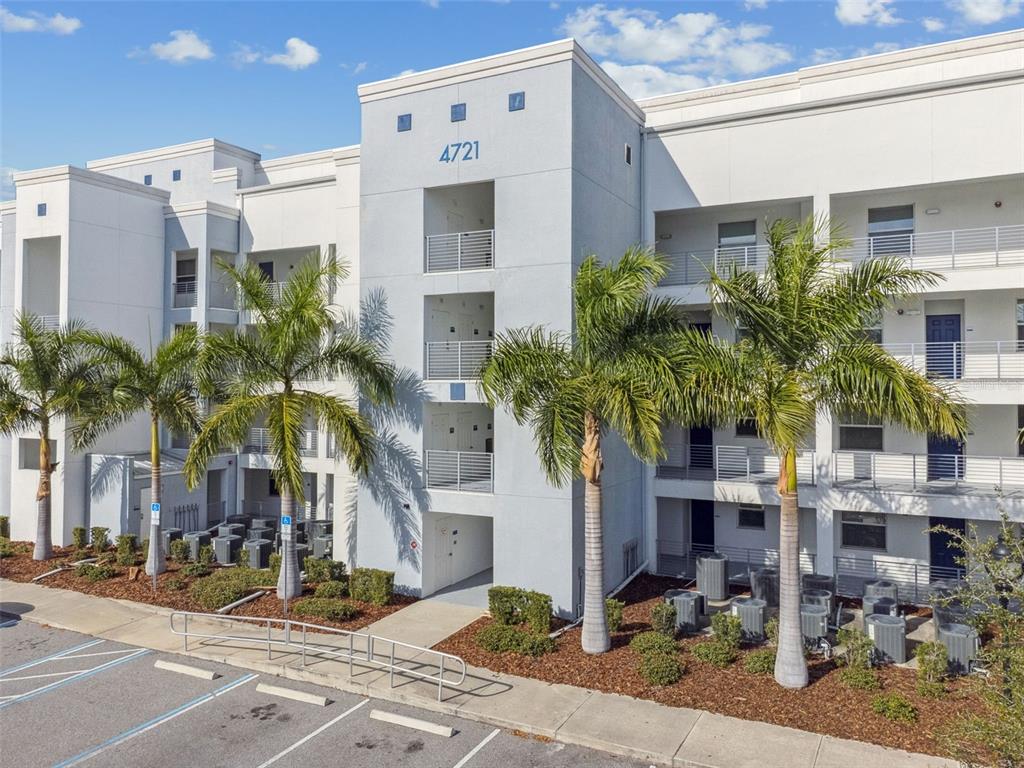 An exterior view of a multi-story apartment building with palm trees and a parking lot — 4721 CLOCK TOWER DRIVE UNIT 107, KISSIMMEE, FL