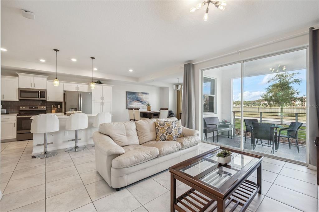 An open-concept living room and kitchen with tile flooring, white cabinetry, and a sliding glass door — 4721 CLOCK TOWER DRIVE UNIT 107, KISSIMMEE, FL