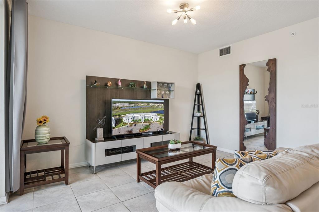 A living room features a television on a media console, a coffee table, and a mirror — 4721 CLOCK TOWER DRIVE UNIT 107, KISSIMMEE, FL