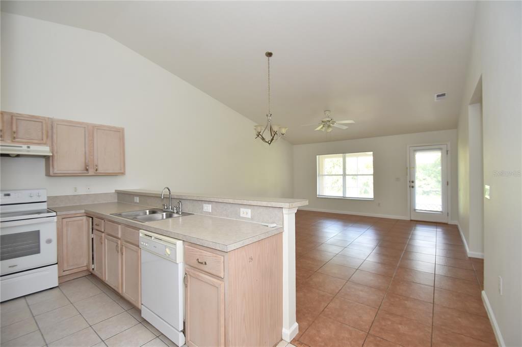 A kitchen with light wood cabinets and white appliances overlooks a tiled living area — 30 ETON LANE, PALM COAST, FL
