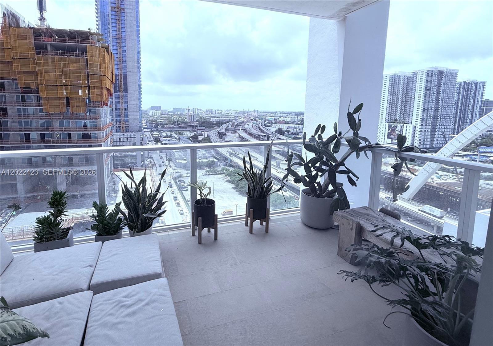 A balcony features potted plants, a wooden bench, and a view of city buildings — 1040 Biscayne Blvd # 1606, Miami FL 33132, MIAMI, FL