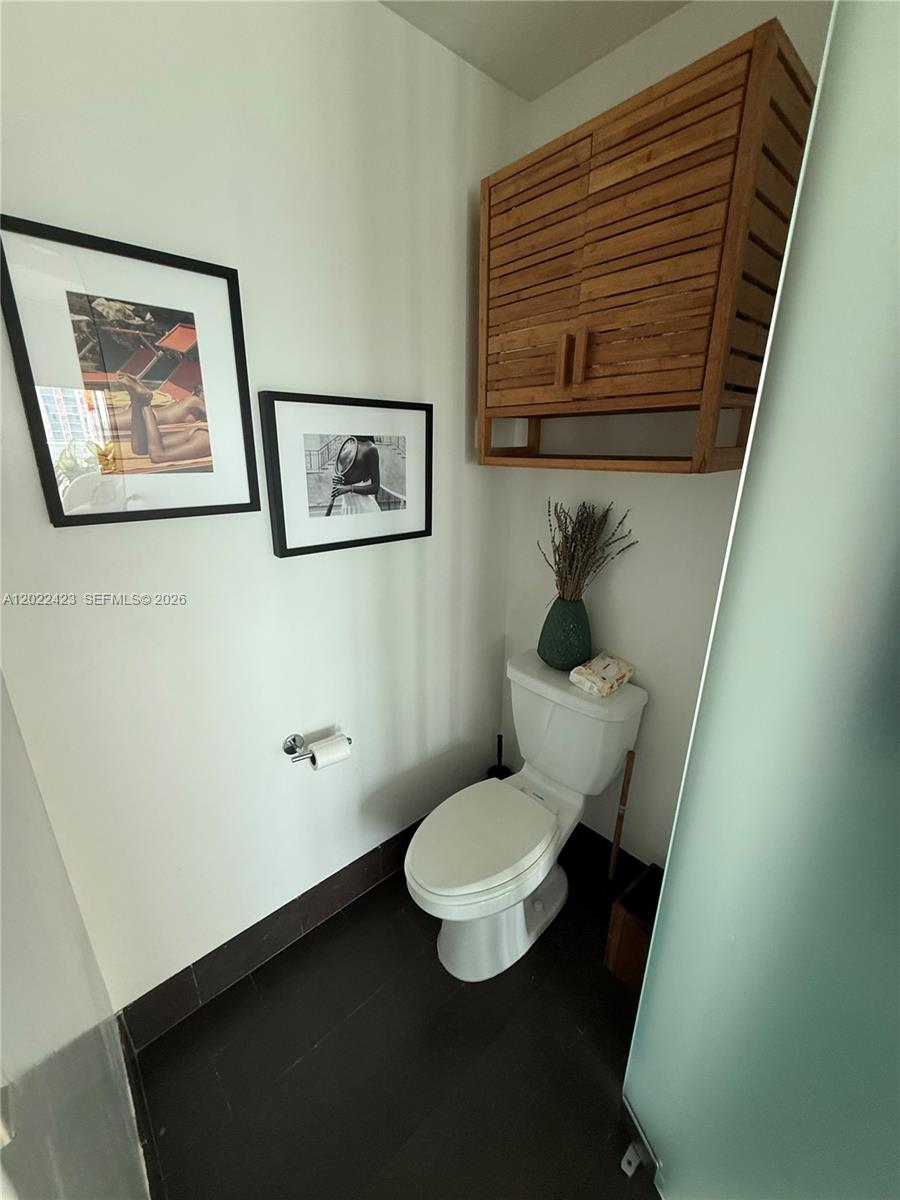 A bathroom features a white toilet, a wooden wall cabinet, and two framed wall pictures — 1040 Biscayne Blvd # 1606, Miami FL 33132, MIAMI, FL