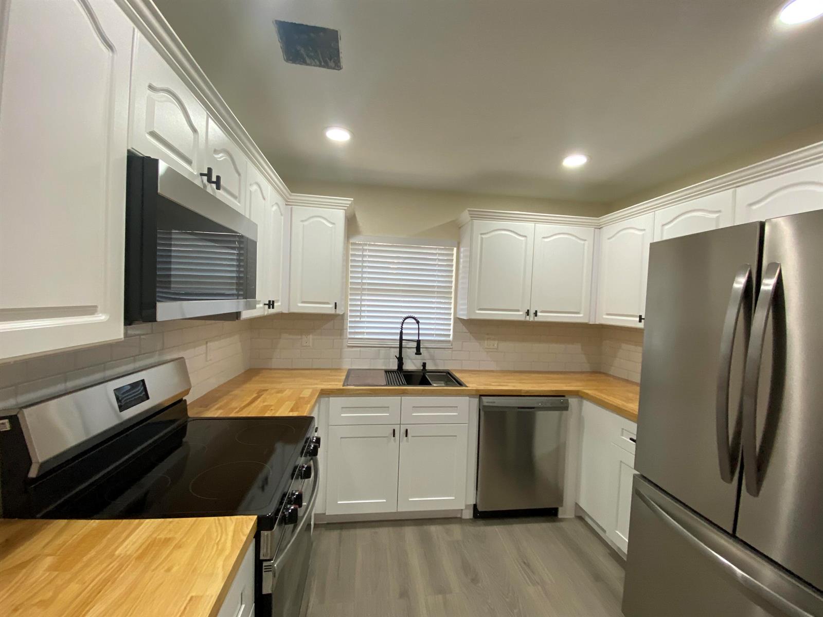 A kitchen features white cabinets, butcher block countertops, stainless steel appliances, and light wood flooring — 176 SW 5th Court, Deerfield Beach FL 33441, DEERFIELD BEACH, FL