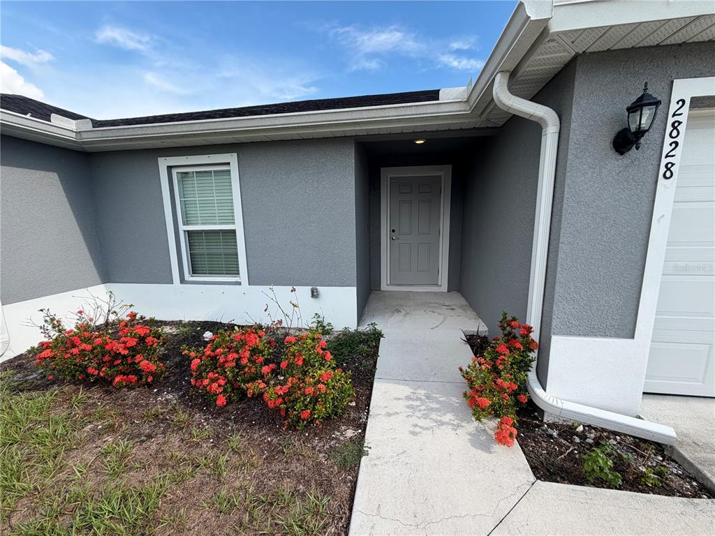 The exterior of a gray house features a front door, a window, and red flowering shrubs — 2828 SW 2ND TERRACE, CAPE CORAL, FL