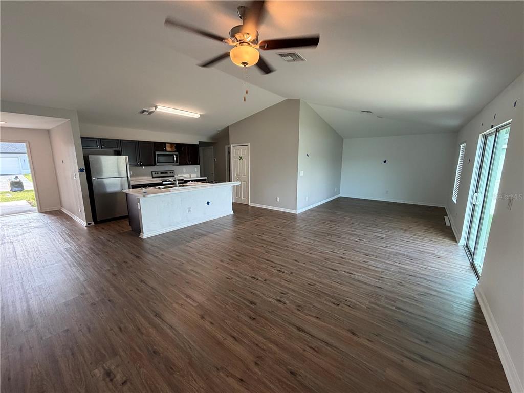 An open-concept living area features wood-look flooring, a kitchen with dark cabinets, and vaulted ceilings — 2828 SW 2ND TERRACE, CAPE CORAL, FL