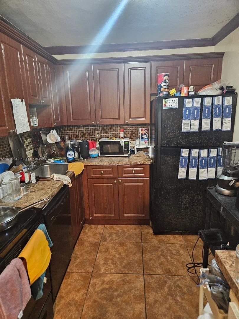 A kitchen features dark wood cabinets, granite countertops, a black refrigerator, and tiled flooring — 18755 NW 62nd Ave # 101, Hialeah FL 33015, HIALEAH, FL