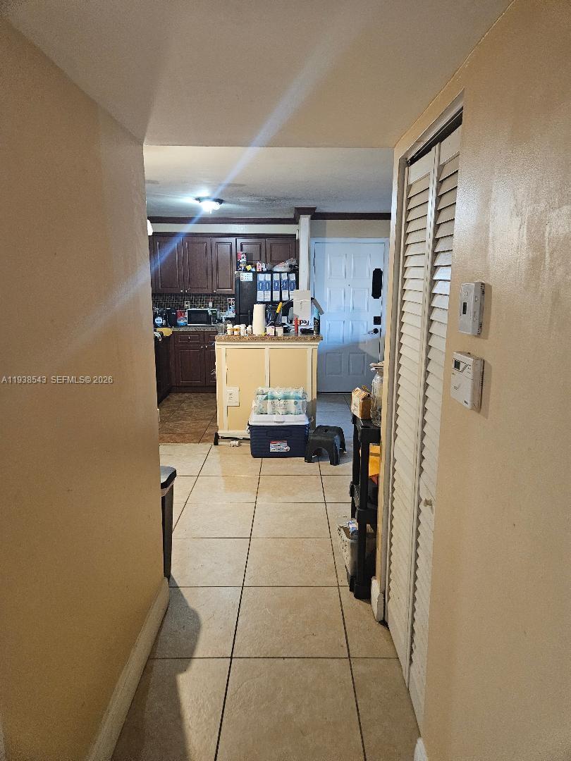 A hallway with tile flooring leads to a kitchen featuring dark cabinets and an island — 18755 NW 62nd Ave # 101, Hialeah FL 33015, HIALEAH, FL