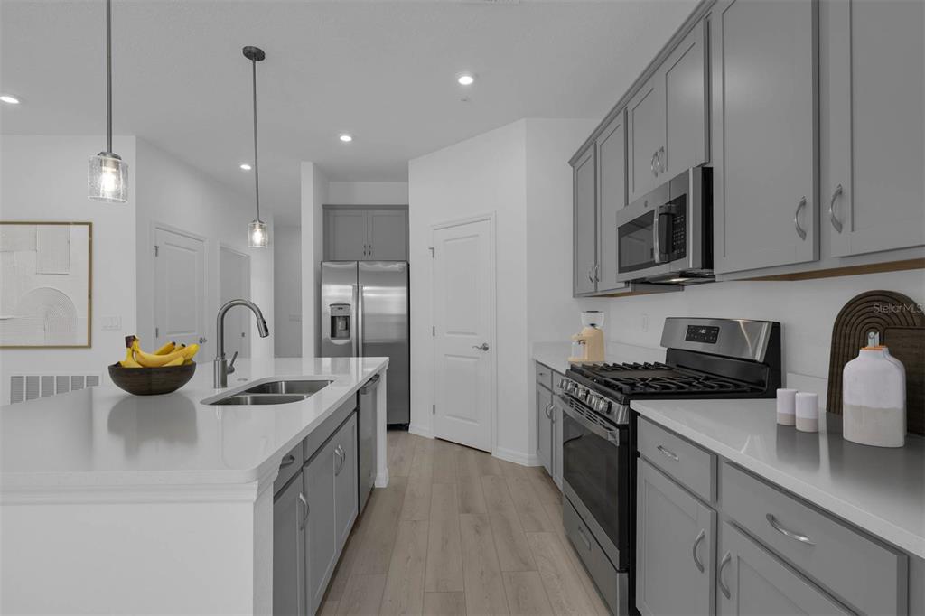 A modern kitchen features gray cabinets, stainless steel appliances, and a white quartz island countertop — 33192 CONTENTMENT WAY, WESLEY CHAPEL, FL