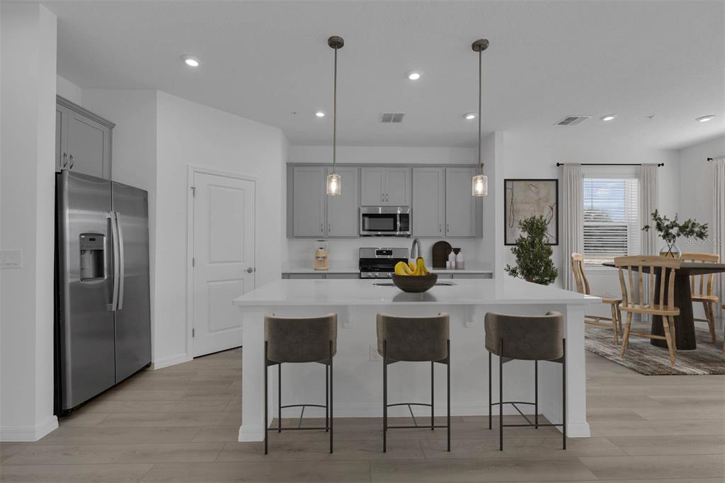 A modern kitchen features gray cabinets, stainless steel appliances, a white island, and bar stools — 33192 CONTENTMENT WAY, WESLEY CHAPEL, FL