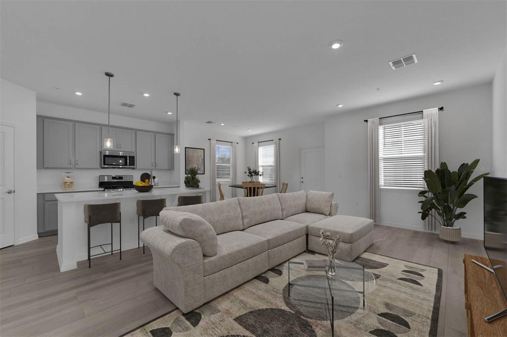 An open-concept living room and kitchen featuring gray cabinetry, a sectional sofa, and wood flooring — 33192 CONTENTMENT WAY, WESLEY CHAPEL, FL