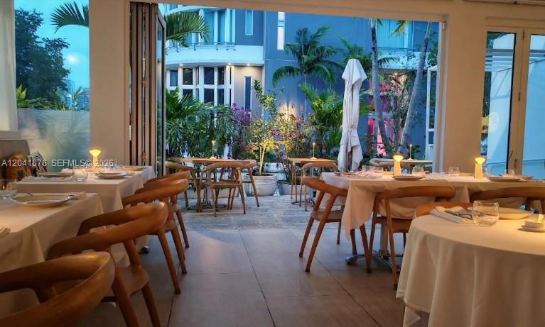 A restaurant dining room features white-clothed tables and wooden chairs opening to an outdoor patio — MIAMI, FL