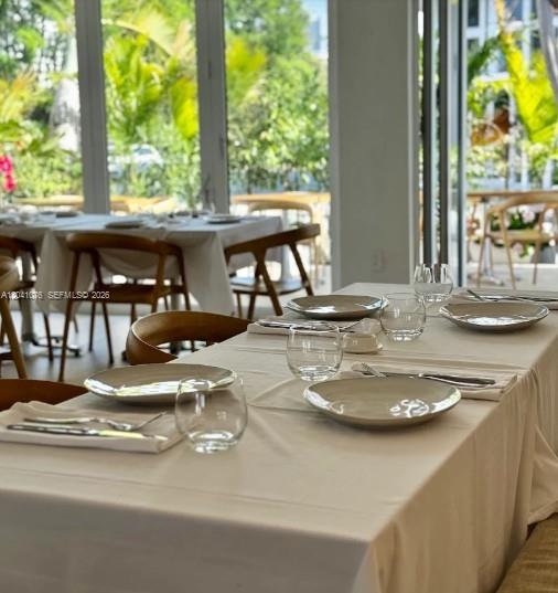 A dining room features tables set with white tablecloths, plates, and glasses near large windows — MIAMI, FL