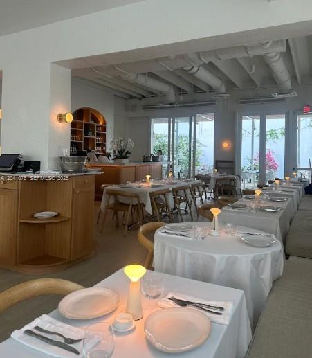 A dining room features white tablecloths, modern table lamps, and exposed white ceiling pipes — MIAMI, FL