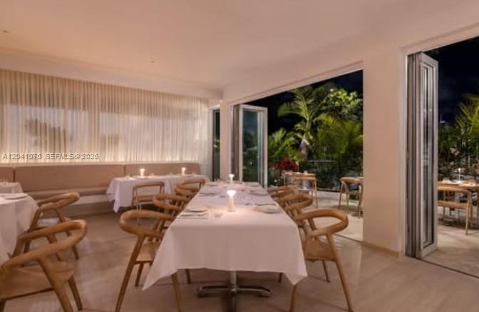 A dining room with white tablecloths, wooden chairs, and large glass doors opening to greenery — MIAMI, FL