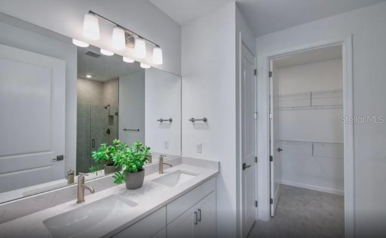 A modern bathroom features a double vanity with a large mirror and an adjacent walk-in closet — 1620 TAVIRA PLACE, ENGLEWOOD, FL