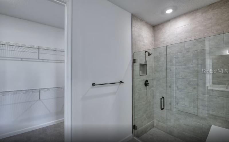 A bathroom features a glass-enclosed tiled shower next to an open walk-in closet — 1620 TAVIRA PLACE, ENGLEWOOD, FL