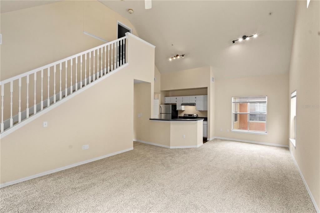 A living room with beige carpet, a staircase, and an open kitchen with white cabinets — 6021 WESTGATE DRIVE UNIT 823, ORLANDO, FL