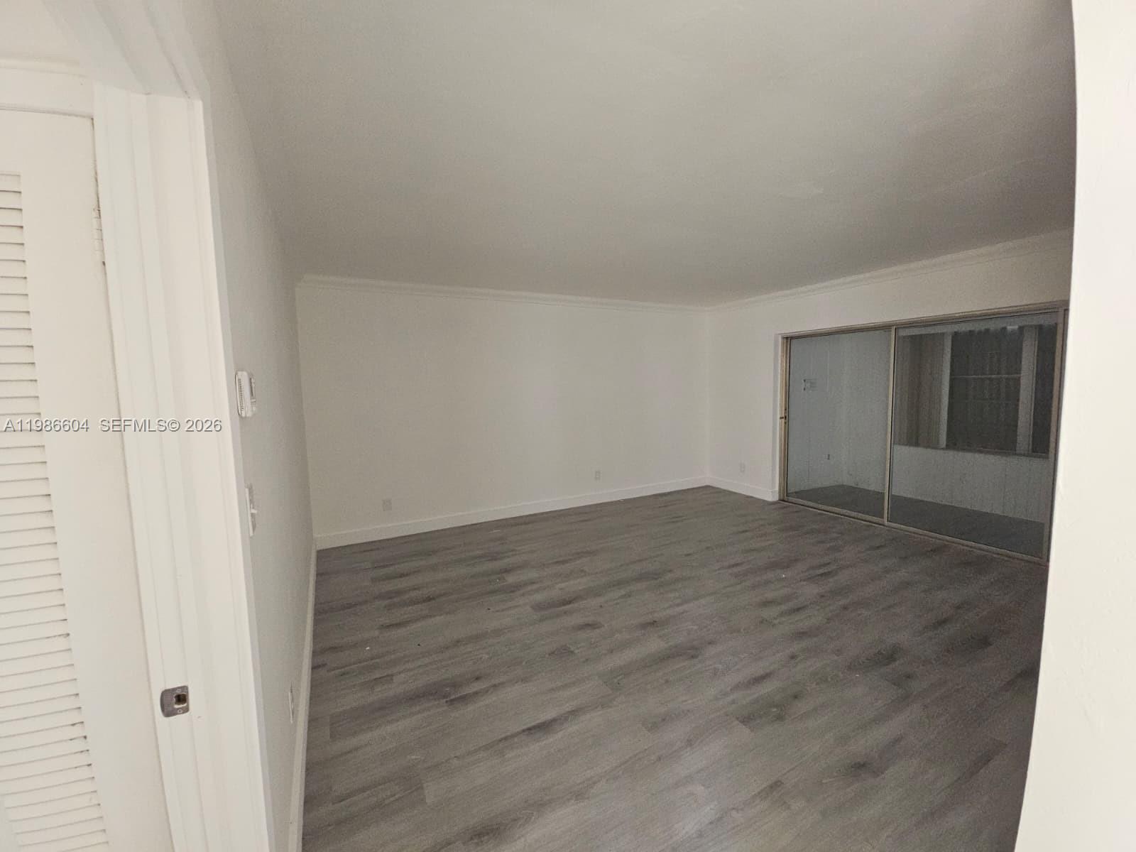 An empty room features gray wood-look flooring, white walls, and a large sliding glass door — 11287 SW 169th St # V41032, Miami FL 33157, MIAMI, FL