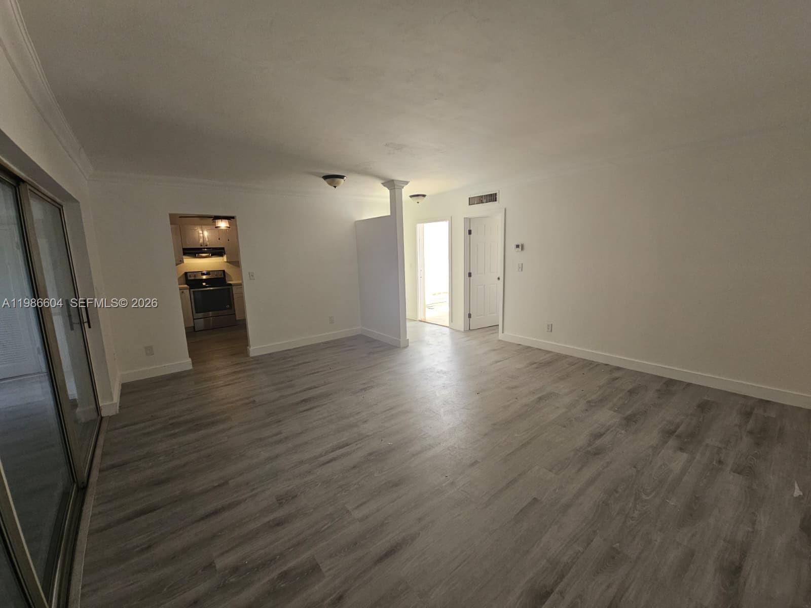 An open living area features white walls, gray wood-look flooring, and a view into the kitchen — 11287 SW 169th St # V41032, Miami FL 33157, MIAMI, FL