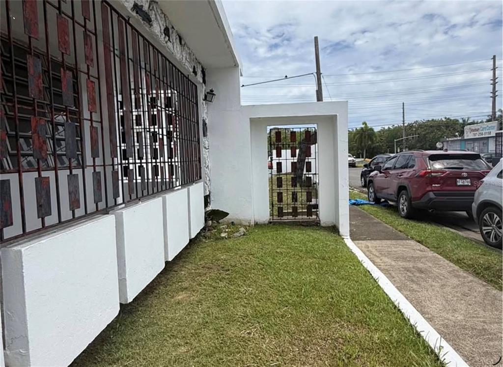 A white exterior wall with metal security bars and a gated entrance next to a driveway — . ACACIA UNIT A37, CANOVANAS, PR