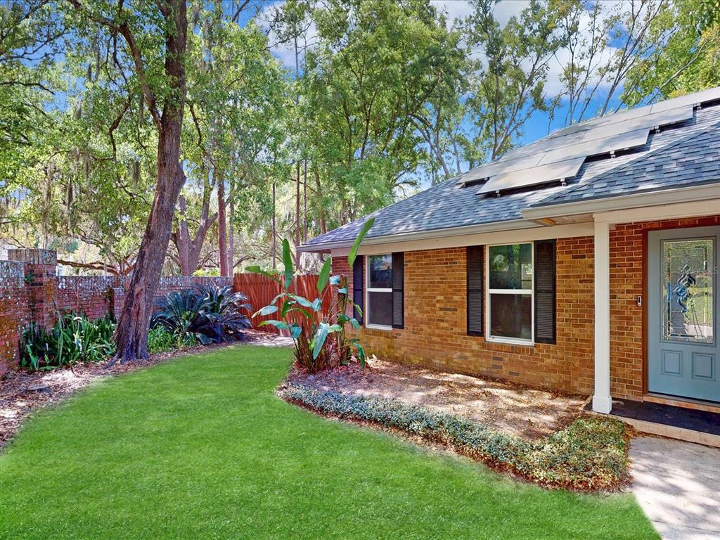 A brick house exterior features a green lawn, solar panels, and a wooden fence — 432 WILDERNESS DRIVE, LONGWOOD, FL