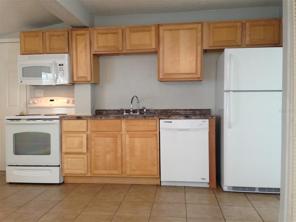 A kitchen features light wood cabinets, white appliances, a dark countertop, and tiled flooring — 1328 CLOVERLAWN AVENUE UNIT B, ORLANDO, FL