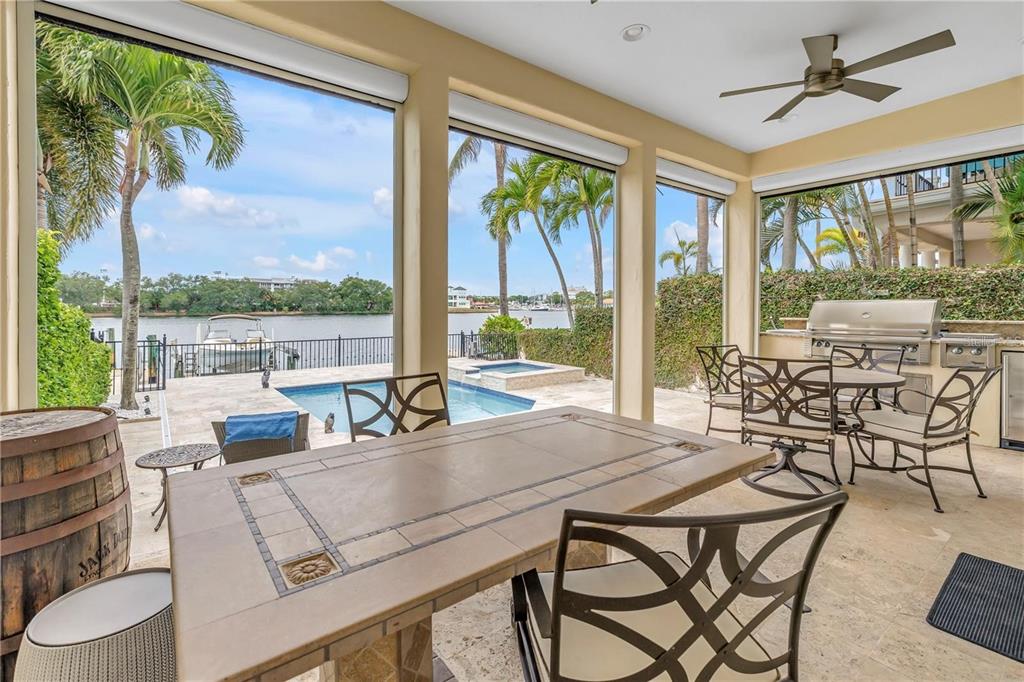 A covered patio features a dining table, outdoor kitchen, swimming pool, and waterfront views — 1133 ABBEYS WAY, TAMPA, FL