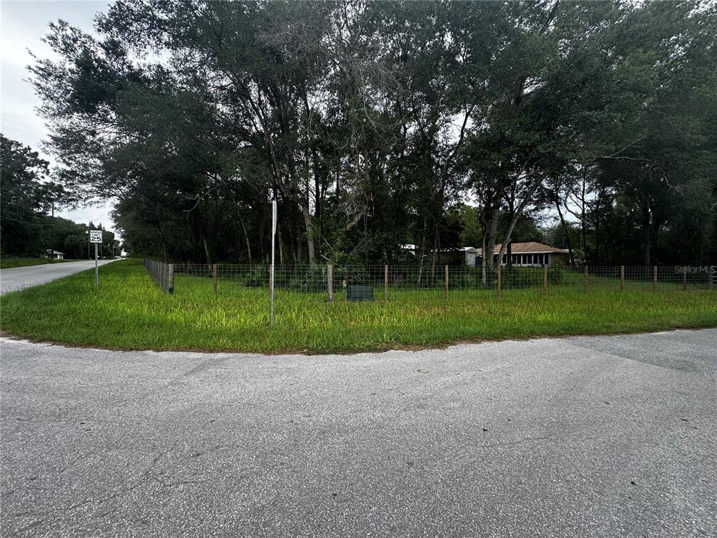A fenced, wooded corner lot with a house visible in the background — 719 S ARLENE AVENUE, INVERNESS, FL