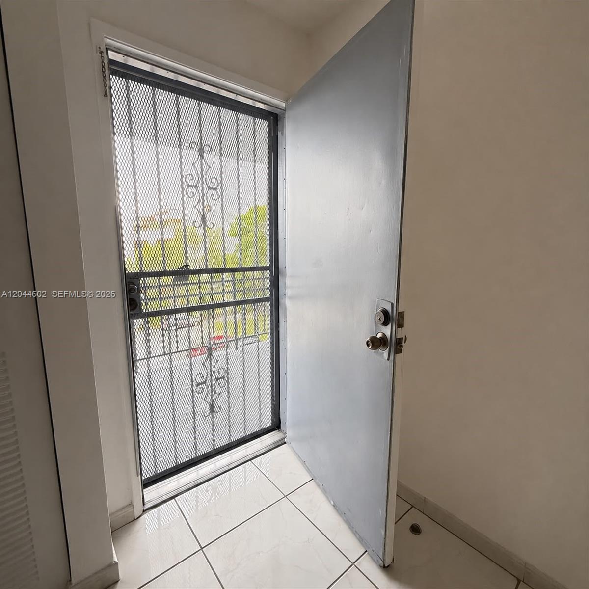 An open gray door reveals a metal security screen door leading to an outdoor area — MIAMI, FL
