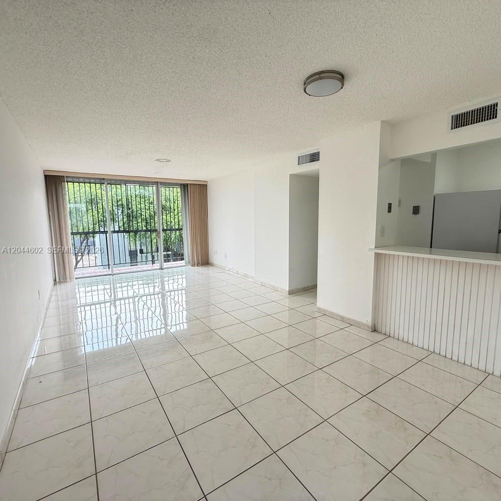 An empty living room features white tile flooring, a breakfast bar, and a sliding glass door — MIAMI, FL