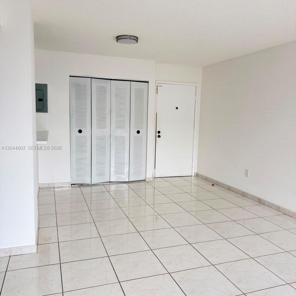 An empty room features white walls, tiled flooring, a closet with louvered doors, and an entrance — MIAMI, FL