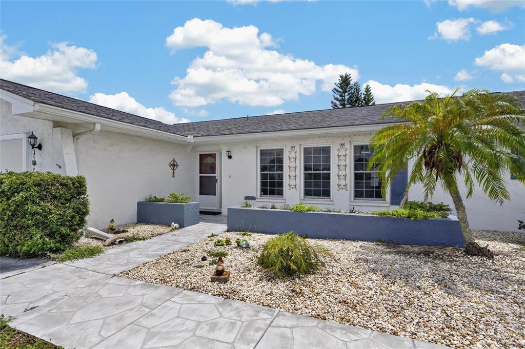 The exterior of a white house features a stone walkway, gravel landscaping, and a palm tree — 1743 COCO PALM CIRCLE, SUN CITY CENTER, FL