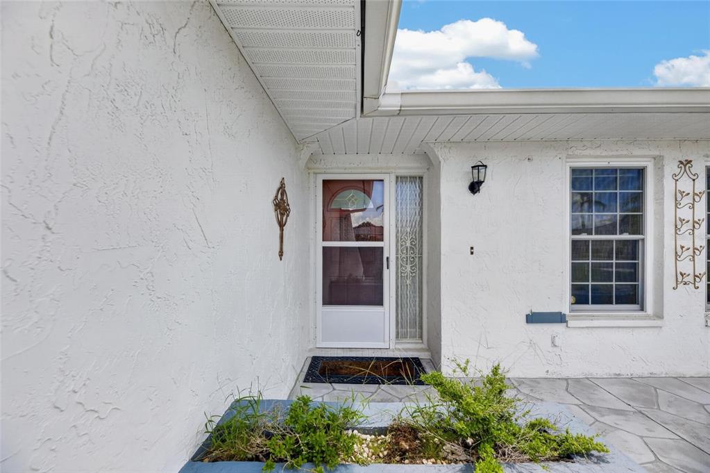 A white stucco house exterior features a front door with a storm door and window — 1743 COCO PALM CIRCLE, SUN CITY CENTER, FL