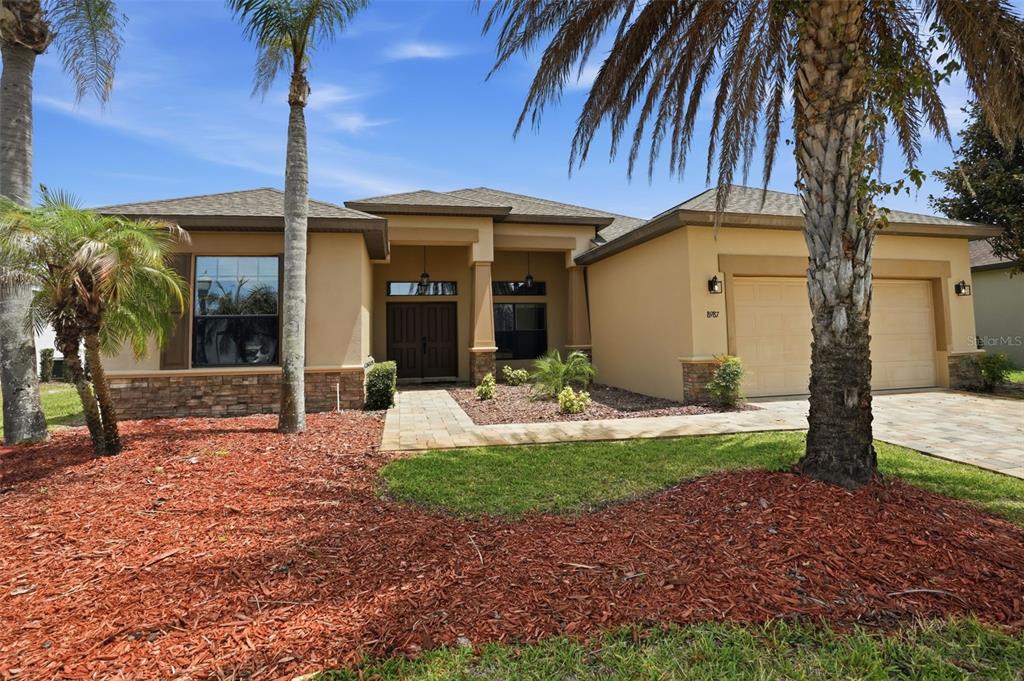 A single-story house with a tan stucco exterior, stone accents, and a two-car garage — 8987 MISSISSIPPI RUN, WEEKI WACHEE, FL