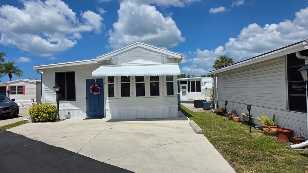 A white manufactured home with a blue front door and a concrete driveway — 1674 UNIVERSITY PKWY LOT 129, SARASOTA, FL