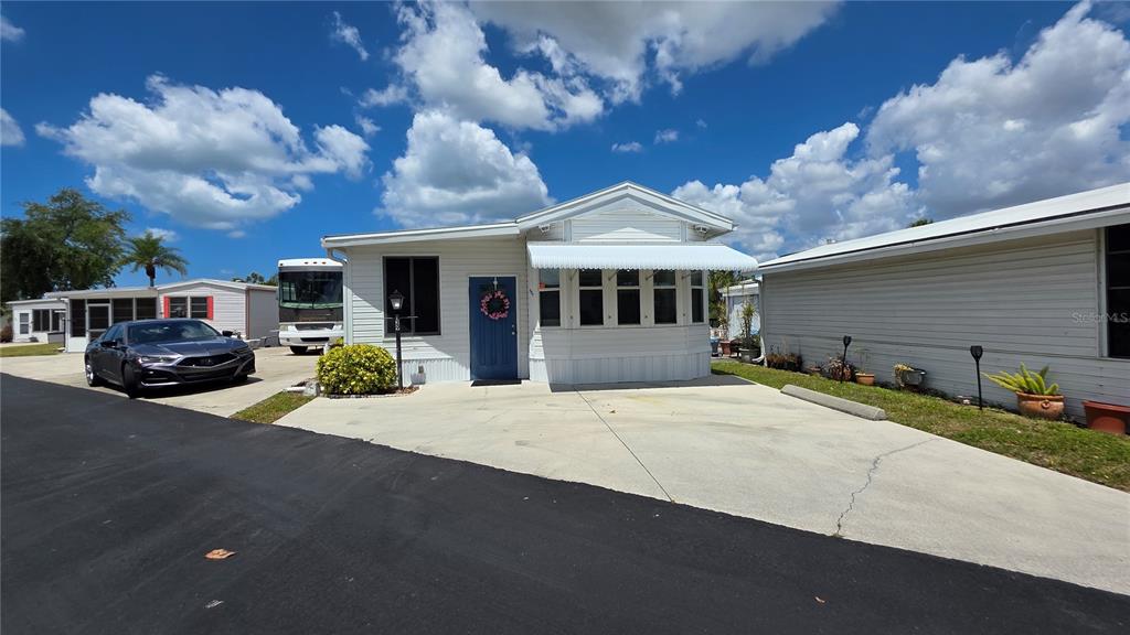 A white manufactured home features a blue front door, a concrete driveway, and a carport — 1674 UNIVERSITY PKWY LOT 129, SARASOTA, FL