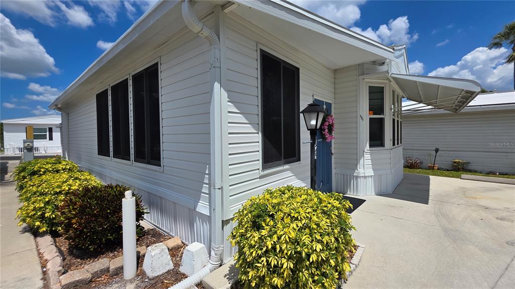 The exterior of a white mobile home features a blue door and landscaped bushes — 1674 UNIVERSITY PKWY LOT 129, SARASOTA, FL
