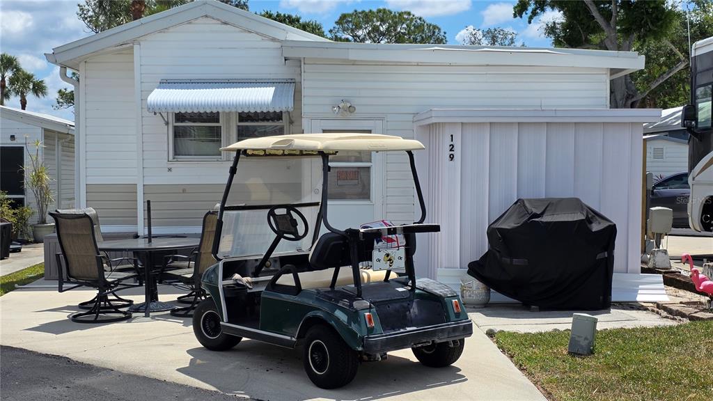 A golf cart sits on a concrete patio in front of a white mobile home — 1674 UNIVERSITY PKWY LOT 129, SARASOTA, FL