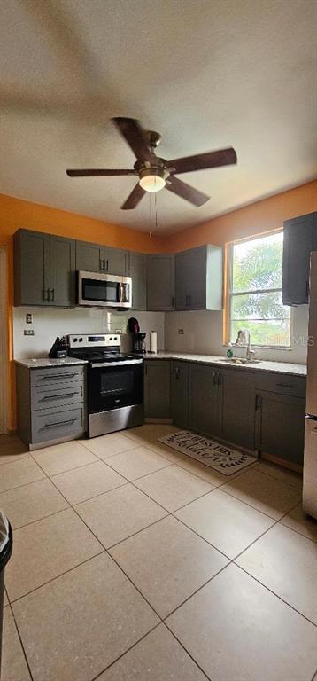 A kitchen features gray cabinets, stainless steel appliances, tile flooring, and an orange accent wall — Apt A-2 Ponciana Condo CARR 413 KM.4.1, RINCON, PR