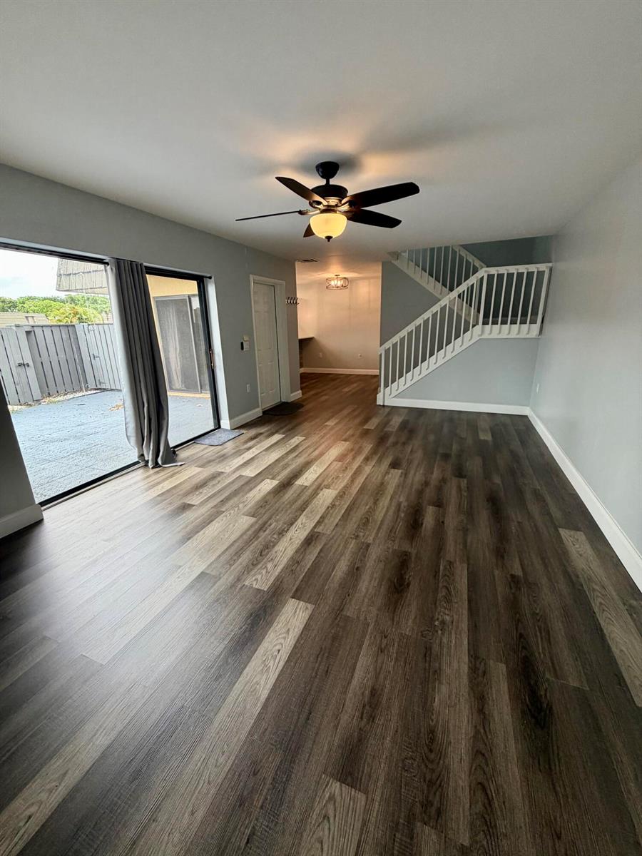 A living room with wood-look flooring, a ceiling fan, a staircase, and a sliding glass door — 1611 16th Way, West Palm Beach FL 33407, WEST PALM BEACH, FL