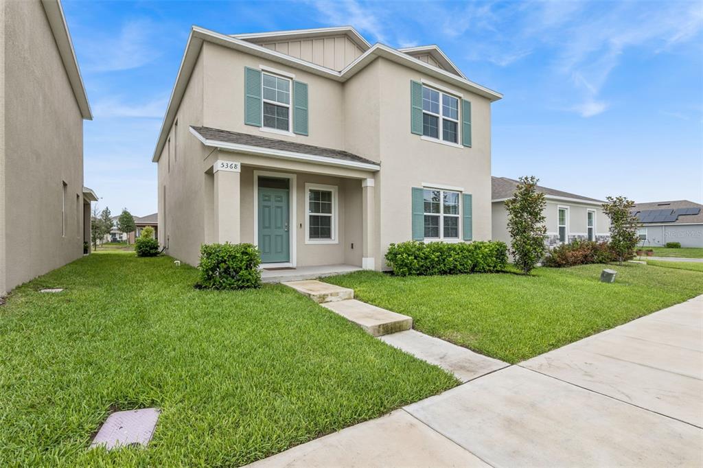 A two-story suburban house with a beige stucco exterior, teal shutters, and a front lawn — 5368 HAYLOFT DRIVE, APOPKA, FL