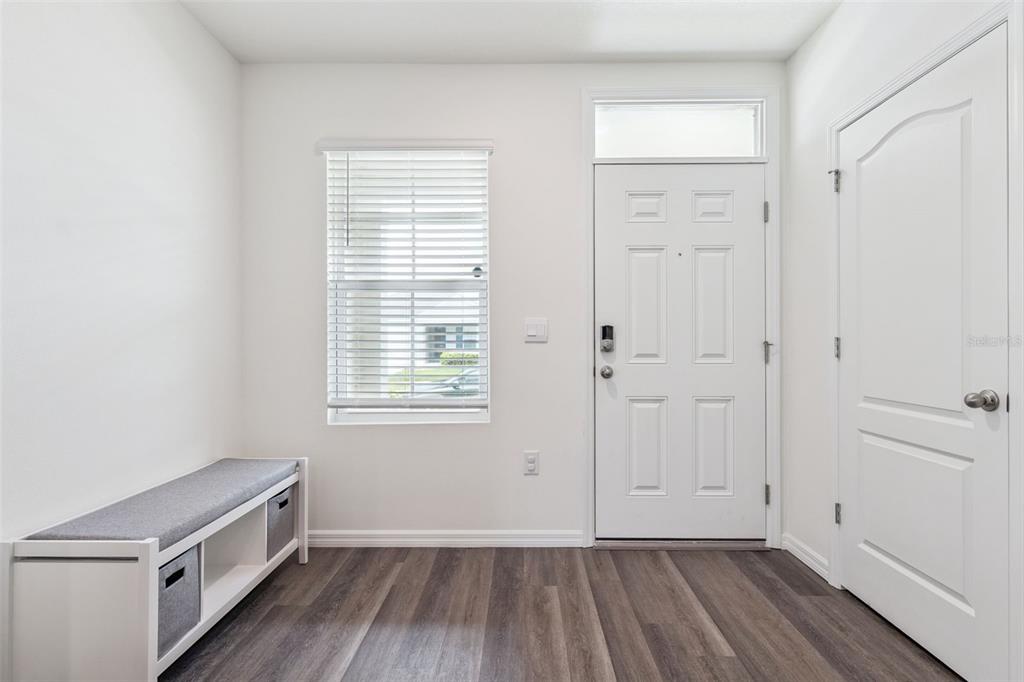 An entryway features a white door, a window with blinds, a storage bench, and wood-look flooring — 5368 HAYLOFT DRIVE, APOPKA, FL