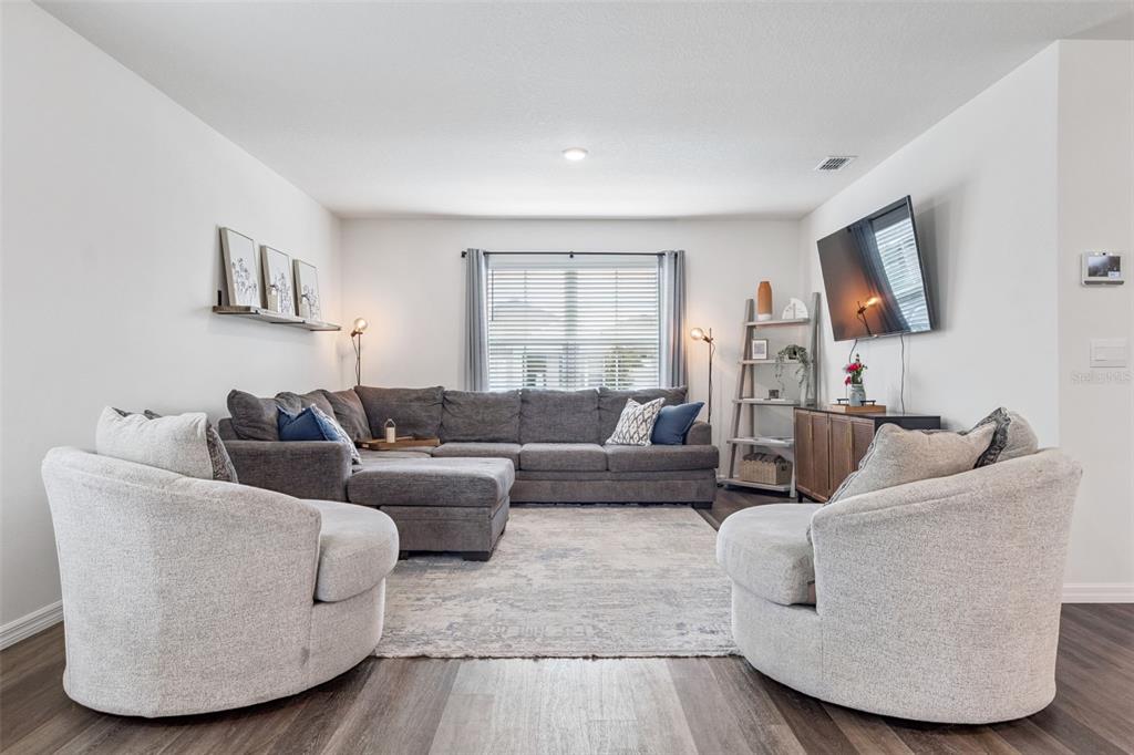 A living room features a grey sectional sofa, two round chairs, and a wall-mounted television — 5368 HAYLOFT DRIVE, APOPKA, FL