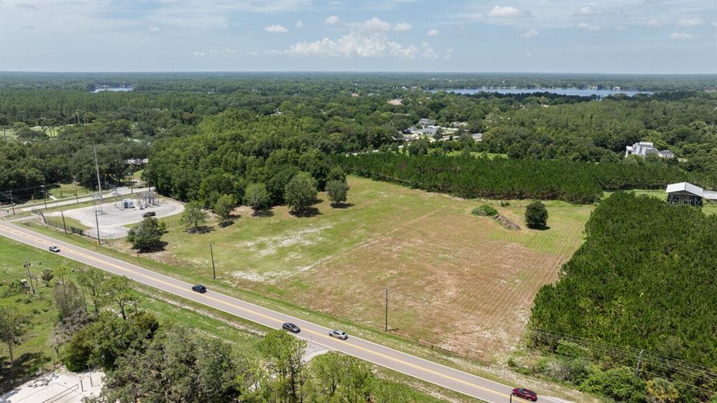 An aerial view shows a large, grassy vacant lot bordering a road and forested area — 18040 GUNN HIGHWAY, ODESSA, FL