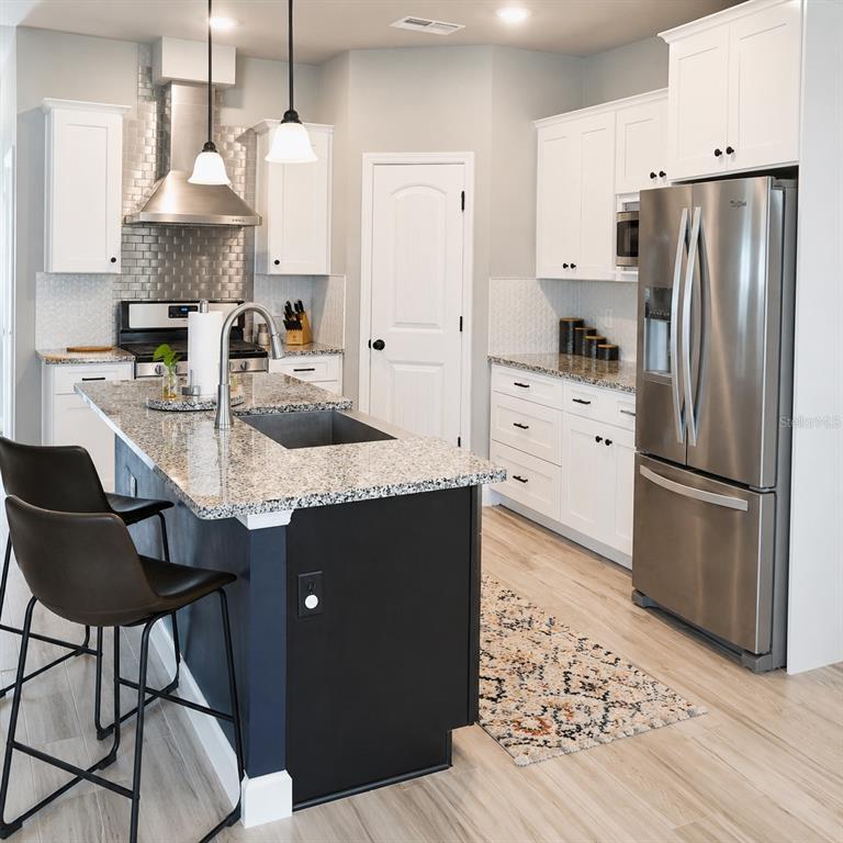 A kitchen features white cabinets, a black island with a granite countertop, and stainless appliances — 1960 SW 247TH WAY, NEWBERRY, FL