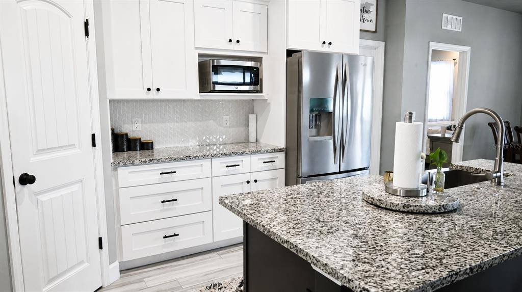 A kitchen features white cabinets, granite countertops, stainless steel appliances, and a dark kitchen island — 1960 SW 247TH WAY, NEWBERRY, FL