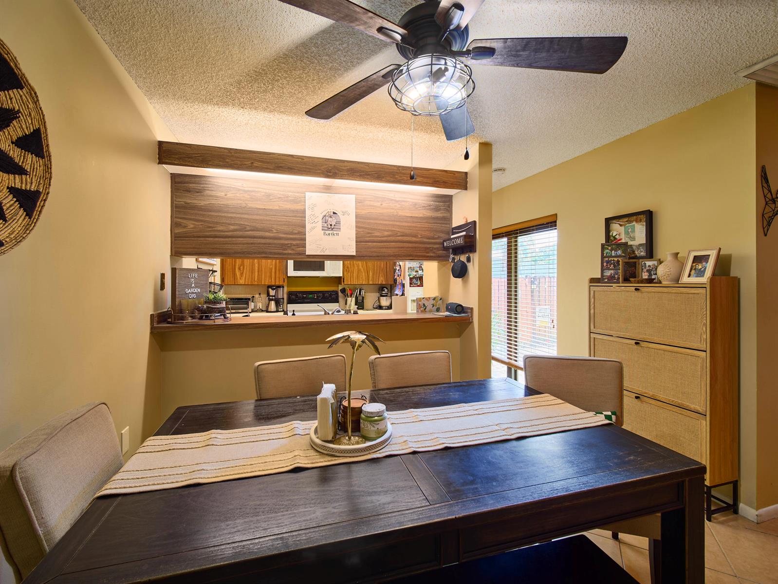A dining room with a dark wood table, upholstered chairs, and a kitchen pass-through window — 3113 31st Way, West Palm Beach FL 33407, WEST PALM BEACH, FL