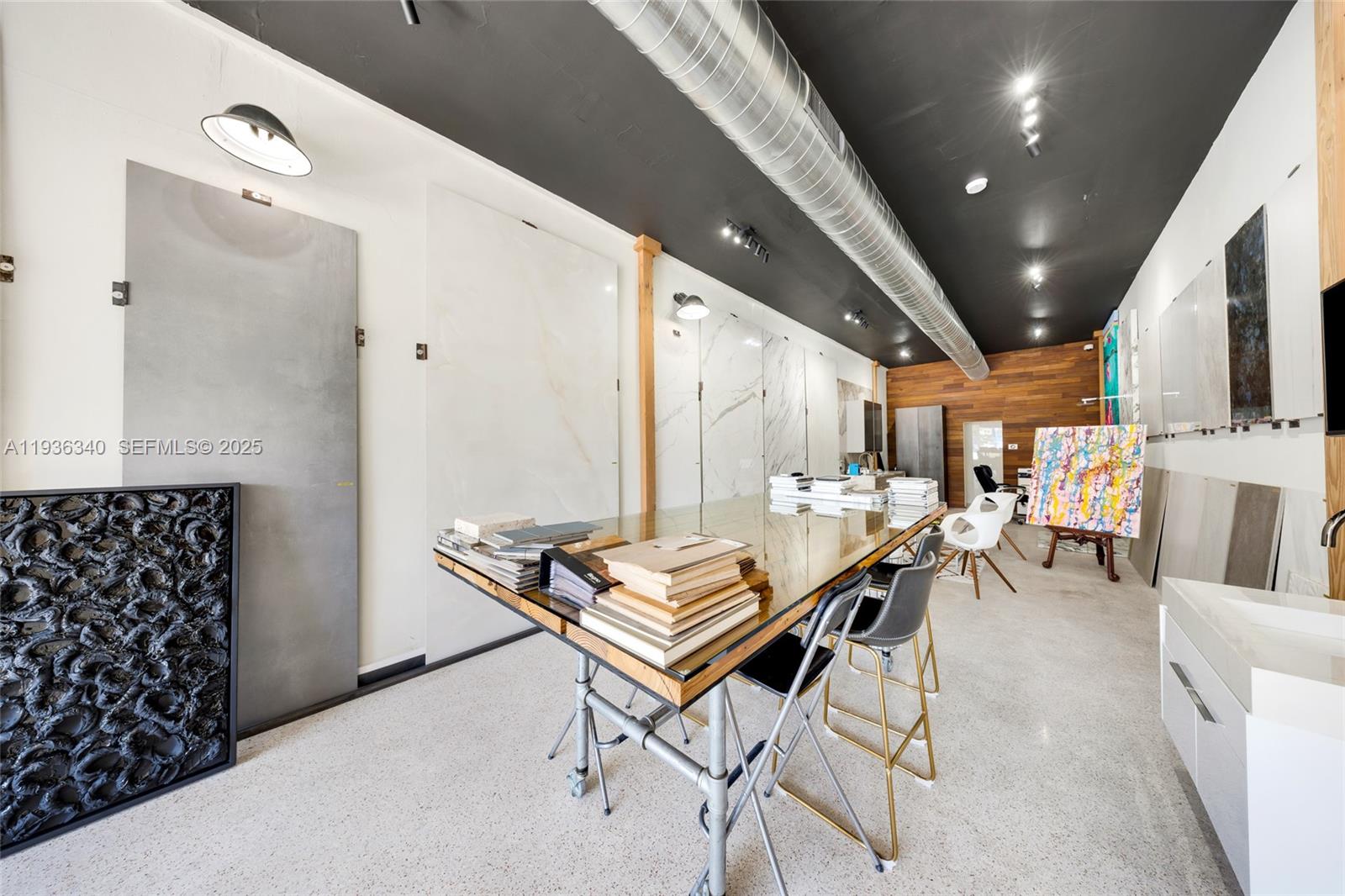 A modern showroom features a large glass-topped table, industrial ductwork, and large-format tile wall displays — 1975 71st St, Miami Beach FL 33141, MIAMI BEACH, FL