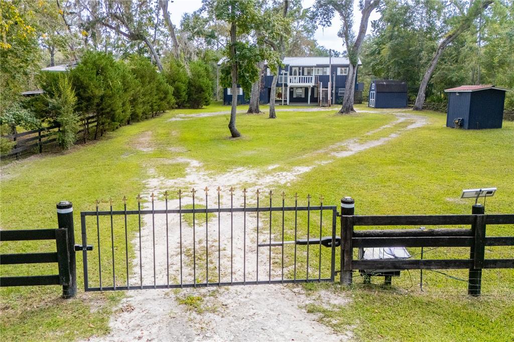 A metal gate opens to a dirt driveway leading toward a two-story house and sheds — 102 NE 931ST STREET, BRANFORD, FL